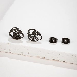 Matte black hollow palm leaf stud earrings set on a textured white stone surface