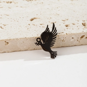 Detail view of a black flying bird pendant with olive branch on a beige stone surface