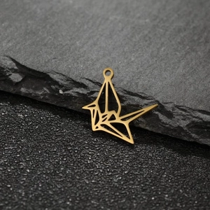 Vue macro d'un pendentif grue en origami doré ajouré posé sur une roche sombre