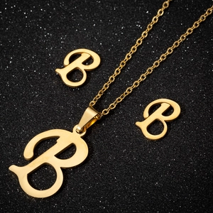 Close-up of golden letter B jewelry set including necklace and studs on black glitter