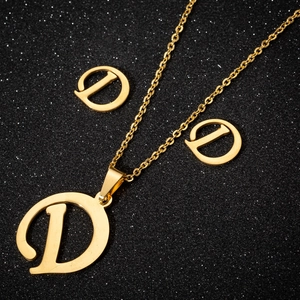 Detailed set of gold letter D pendant necklace and matching stud earrings on black background
