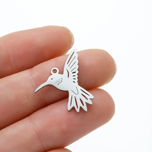 Gros plan détaillé d'un pendentif colibri en acier inoxydable tenu entre les doigts