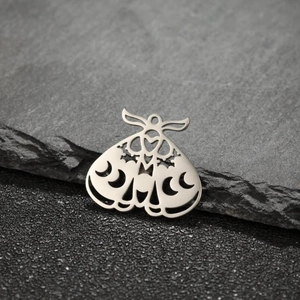Macro shot of silver moth pendant with hollow moon phase design on a textured stone background