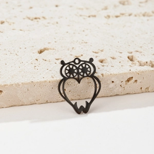 Close-up of black hollow owl pendant with heart body and gear eyes on stone base