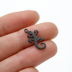 Detailed view of small matte black stainless steel gecko charm held by hand for size reference
