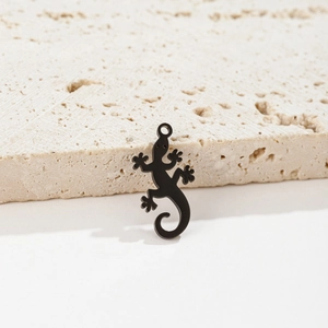 Detailed view of matte black lizard pendant for DIY jewelry on a beige stone surface