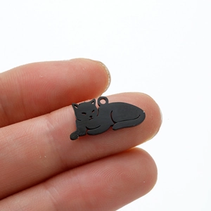 Detailed close-up of a minimalist matte black cat pendant charm on a fingertip