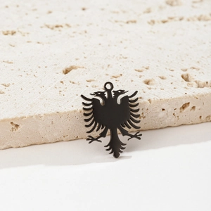 Close-up of a matte black double-headed eagle pendant on a minimalist stone background