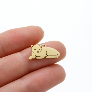 Golden stainless steel lying cat pendant held by fingers to show compact size
