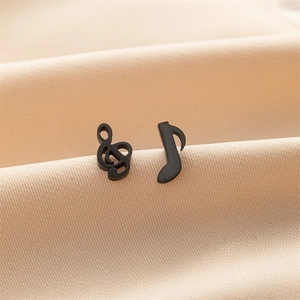 Detail of matte black music note stud earrings on soft beige silk background