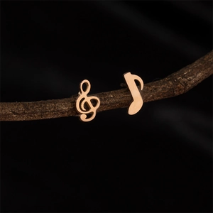 Asymmetric music note stud earrings in rose gold finish on a rustic branch background