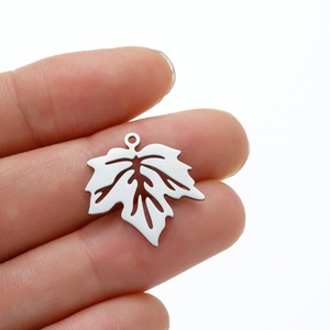 Détail d'un pendentif feuille d'érable argenté ajouré tenu à la main pour l'échelle