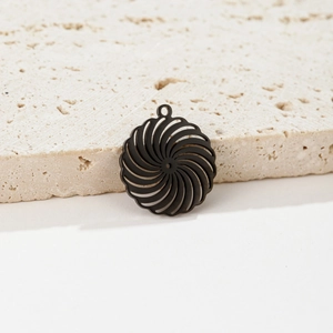 Macro shot of black cutout spiral vortex pendant on a minimalist cream stone