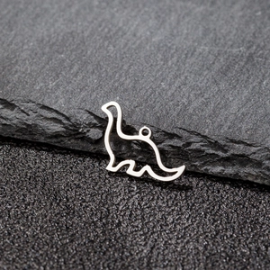 Macro shot of silver cutout dinosaur charm with polished finish on dark rock surface