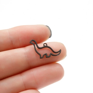 Detail of small black hollow dinosaur pendant held by fingers for jewelry crafting
