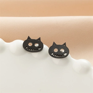Detailed macro view of black cat skull stud earrings on a white ceramic jewelry tray