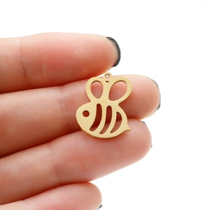 Close-up of a small gold hollow bee pendant for DIY jewelry making held by fingers