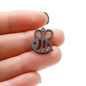 Macro shot of a matte black bee charm held by fingers showing size for DIY jewelry