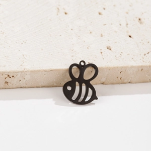Close-up of a black hollowed-out stainless steel bee pendant on a textured stone edge