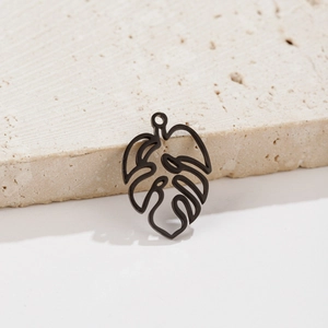 Macro detail of matte black monstera leaf pendant with cutout design on stone