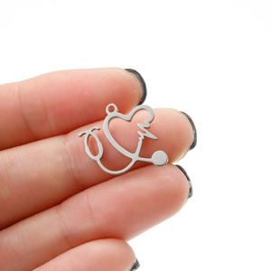 Polished stainless steel stethoscope heart pendant held to show product size and scale