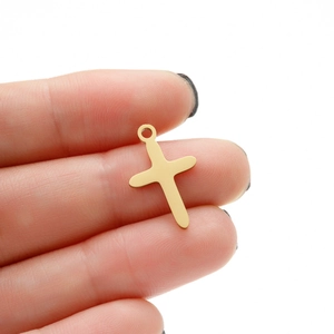 Detailed view of polished gold plated stainless steel cross pendant held in hand