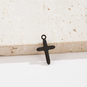Detail of matte black stainless steel cross pendant on beige marble stone texture