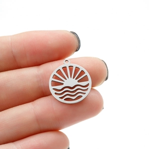 Close-up of a silver hollow round sun and wave pendant held between fingers