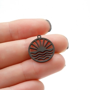 Macro view of black matte wave and sun hollow circular pendant held by fingers