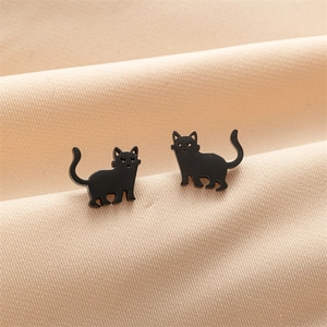 Gros plan de boucles d'oreilles chat noir mat minimalistes sur fond textile beige naturel