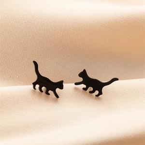 Macro shot of asymmetric black cat stud earrings on beige silk fabric background