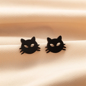 Close-up of matte black cat stud earrings on a smooth beige silk fabric background