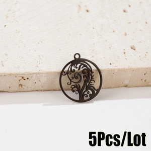 Close-up of 5 black hollowed-out metal leaf pendants for jewelry making on stone