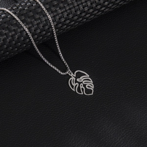 Polished stainless steel monstera leaf pendant necklace on textured black leather surface
