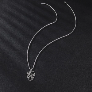 Silver stainless steel monstera leaf pendant necklace on a black textured background