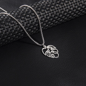 Close-up of a silver monstera leaf pendant on a stainless steel box chain necklace