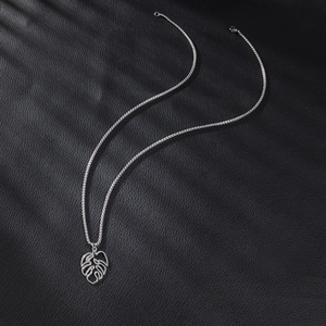 Macro detail of silver monstera leaf pendant necklace on black textured leather surface