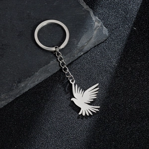 Polished stainless steel flying pigeon keychain with a circular ring on a textured stone
