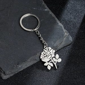 Silver stainless steel rose pendant keychain on a dark textured stone background