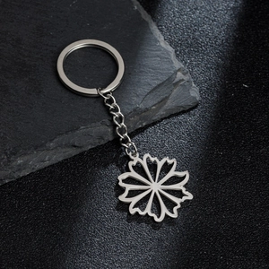 Polished stainless steel daisy petal keychain on a textured black stone surface