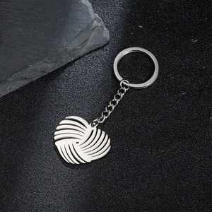Polished stainless steel heart keychain with geometric origami texture on dark stone surface