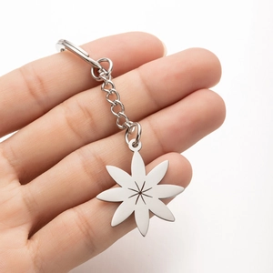 Close-up of silver stainless steel daisy pendant keychain held by hand on white background