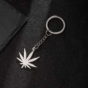 Detailed close-up of a silver stainless steel cannabis leaf keychain on black leather