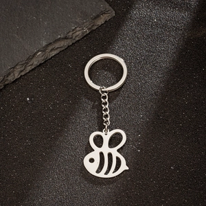Polished stainless steel honey bee pendant keychain on black textured surface