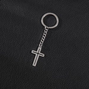 Minimalist silver stainless steel hollow cross pendant keychain on black leather background