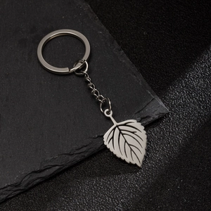 Silver stainless steel leaf keychain with detailed veins on textured stone background