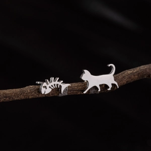 Asymmetric stainless steel cat and fishbone stud earrings shown on a rustic branch