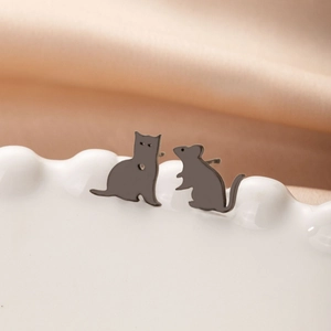 Detail of asymmetric stainless steel cat and mouse stud earrings on a ceramic dish