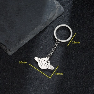 Silver stainless steel Saturn planet keychain with moon and star cutouts on black texture
