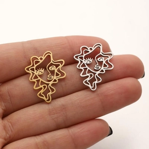 Abstract hollow face charms in gold and silver stainless steel held for size scale